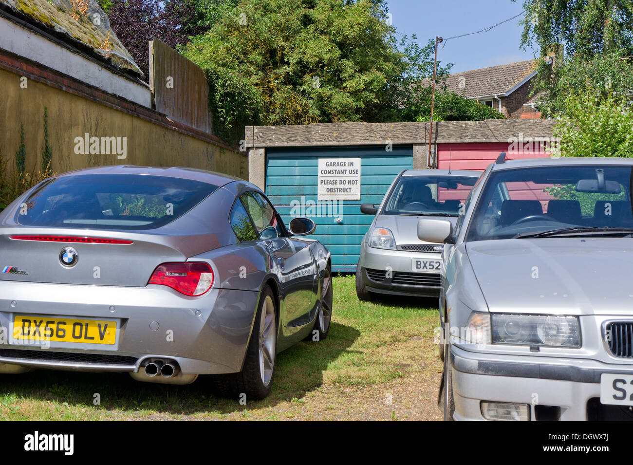 Sign saying 'garage in constant use, please do not obstruct' blocked by three cars. Stock Photo