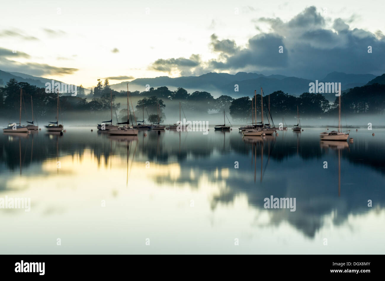 A late evening scene on Windermere lake with distant trees and yachts hidden in the mist and reflected in the water. Stock Photo