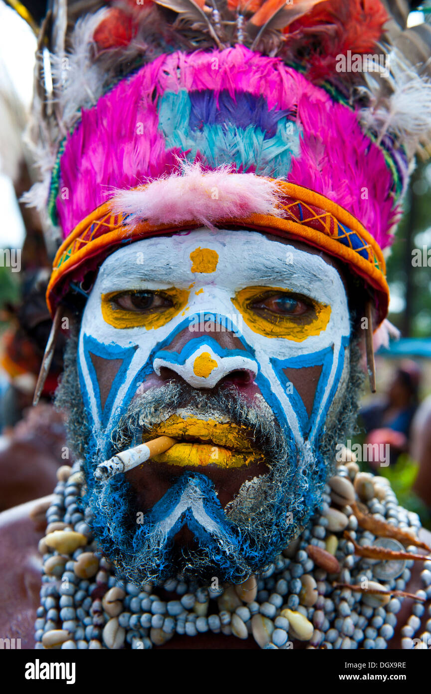 Man in a colourfully decorated costume with face paint and a cigarette at the traditional sing-sing gathering, Hochland Stock Photo