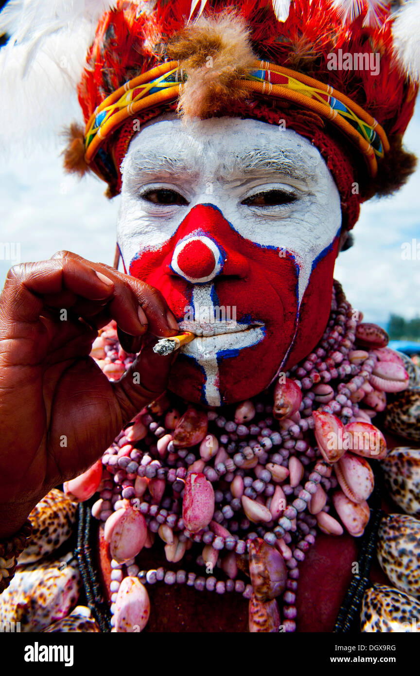 Man in a colourfully decorated costume with face paint smoking a cigarette at the traditional sing-sing gathering, Hochland Stock Photo