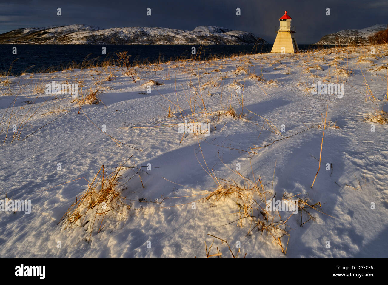 Lighthouse in sunlight against dark sky in winter fjord, Tromsø, Troms, Northern Norway, Norway Stock Photo