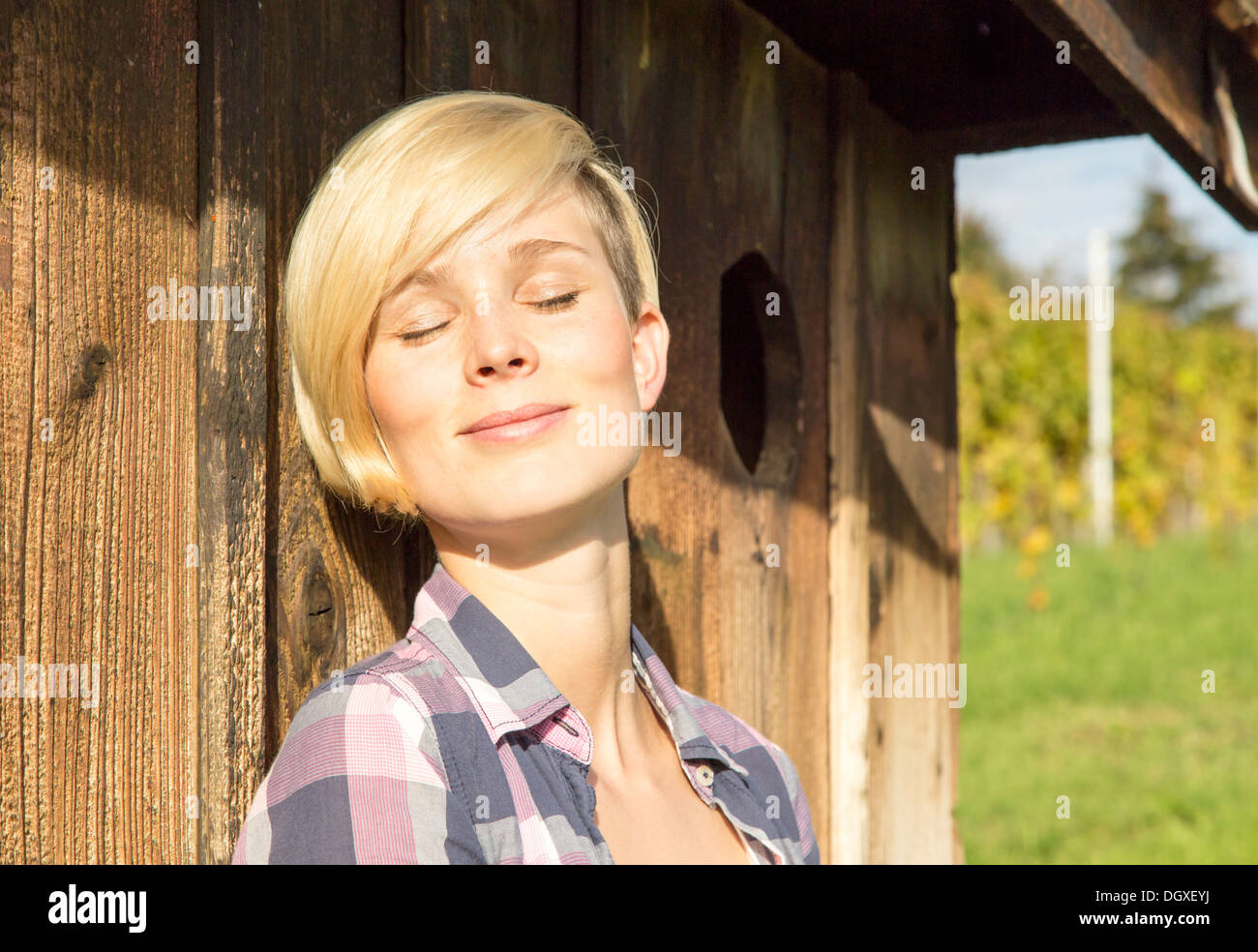 Natural looking woman leans against the wall of a hut and relaxes Stock Photo