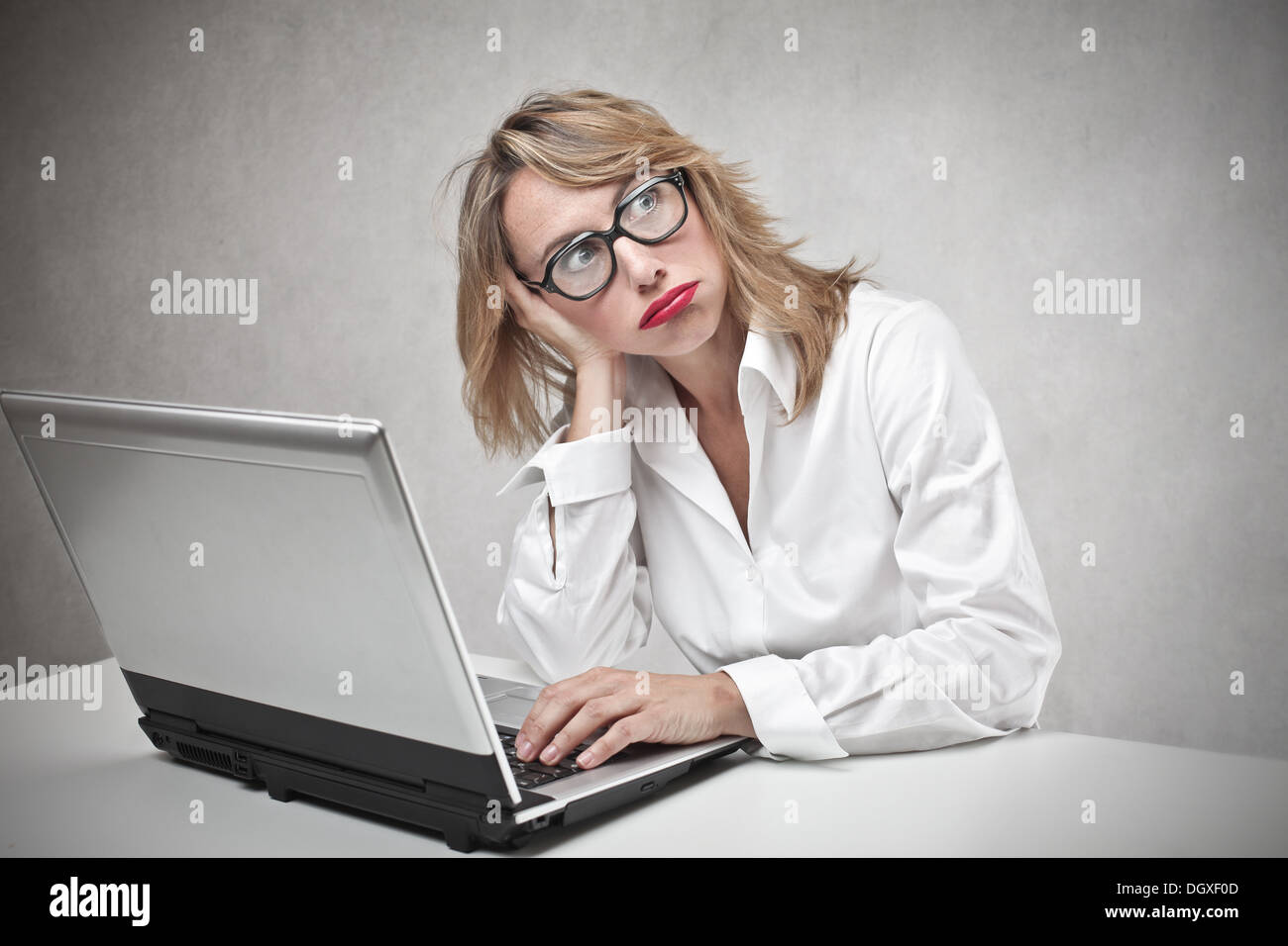 Bored blonde woman with glasses using a laptop Stock Photo