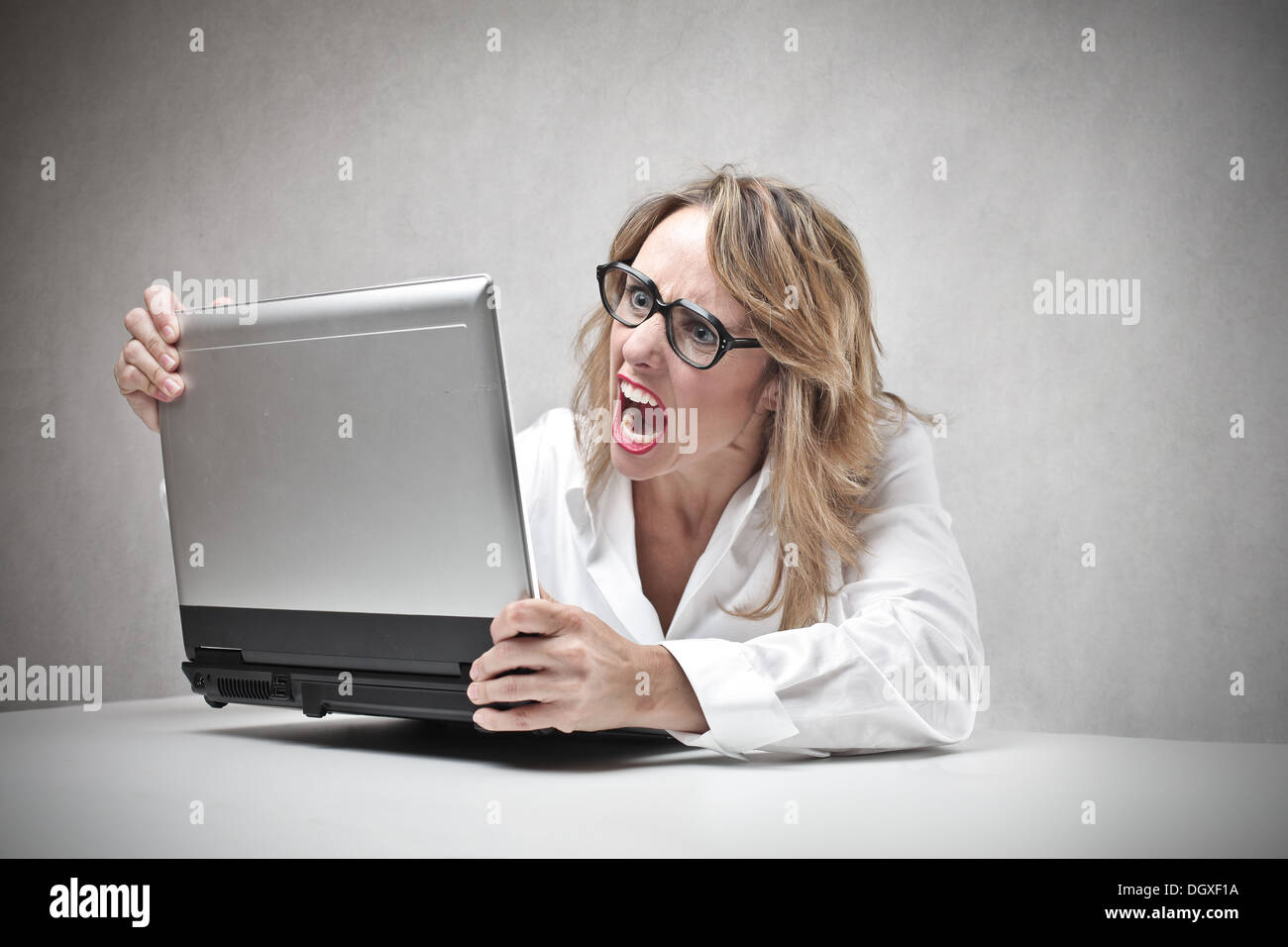 Blonde woman with glasses screaming against a laptop Stock Photo