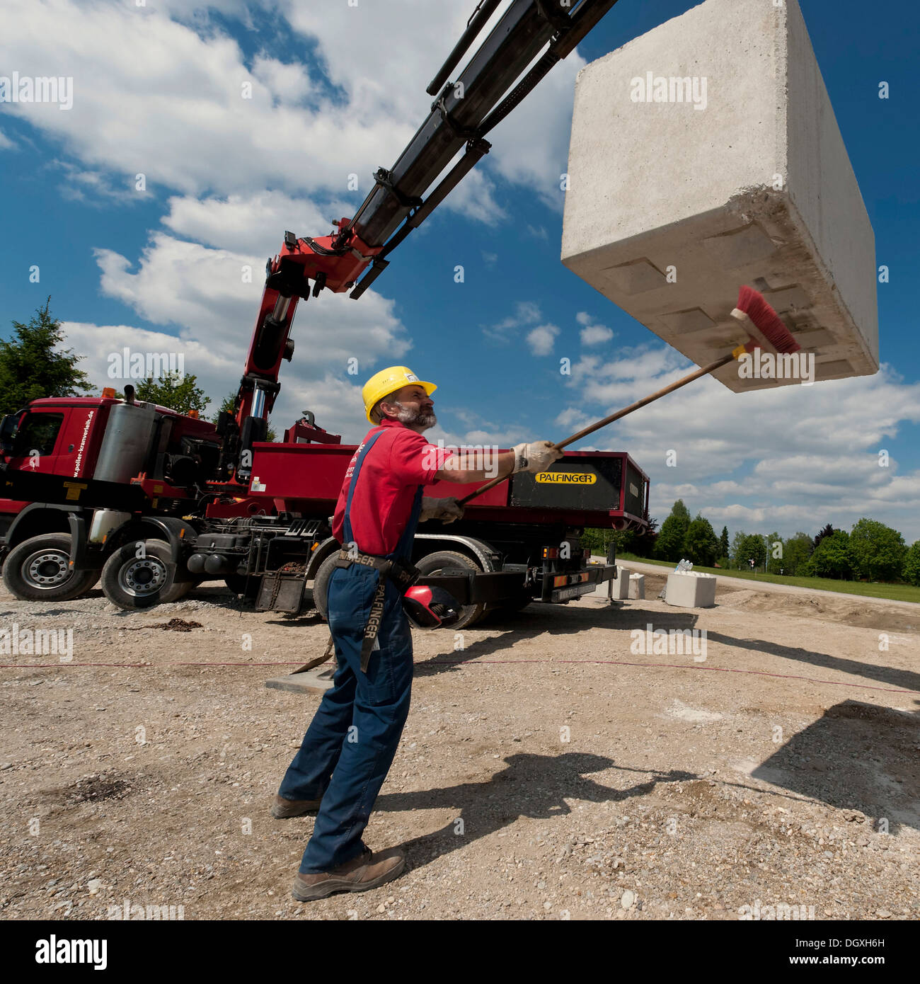 Crane operator cleaning the underside of a concrete block during a building site load test at a construction site in Fridolfing Stock Photo