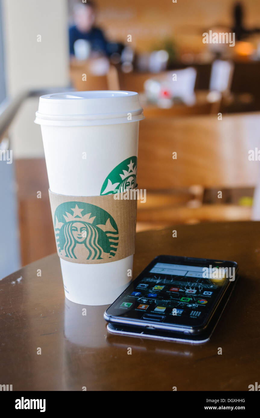 Starbucks coffee cup and a Samsung Galaxy smartphone on a table in a Starbucks. Stock Photo