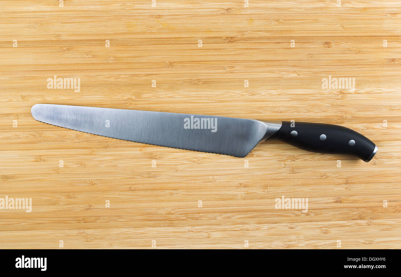 Horizontal photo of large serrated knife on natural bamboo board Stock