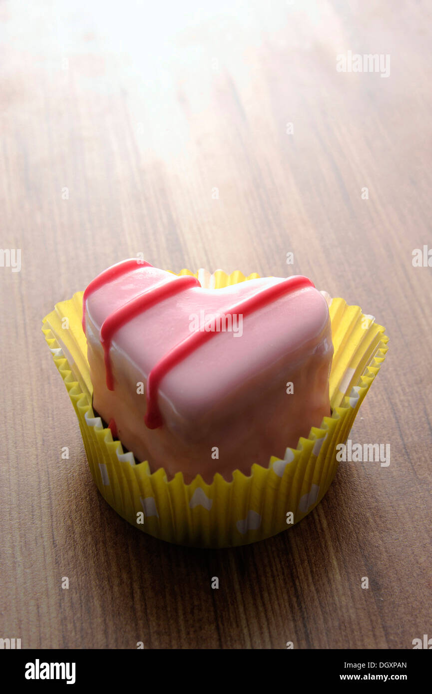 Pink heart-shaped petit four on a wooden surface Stock Photo