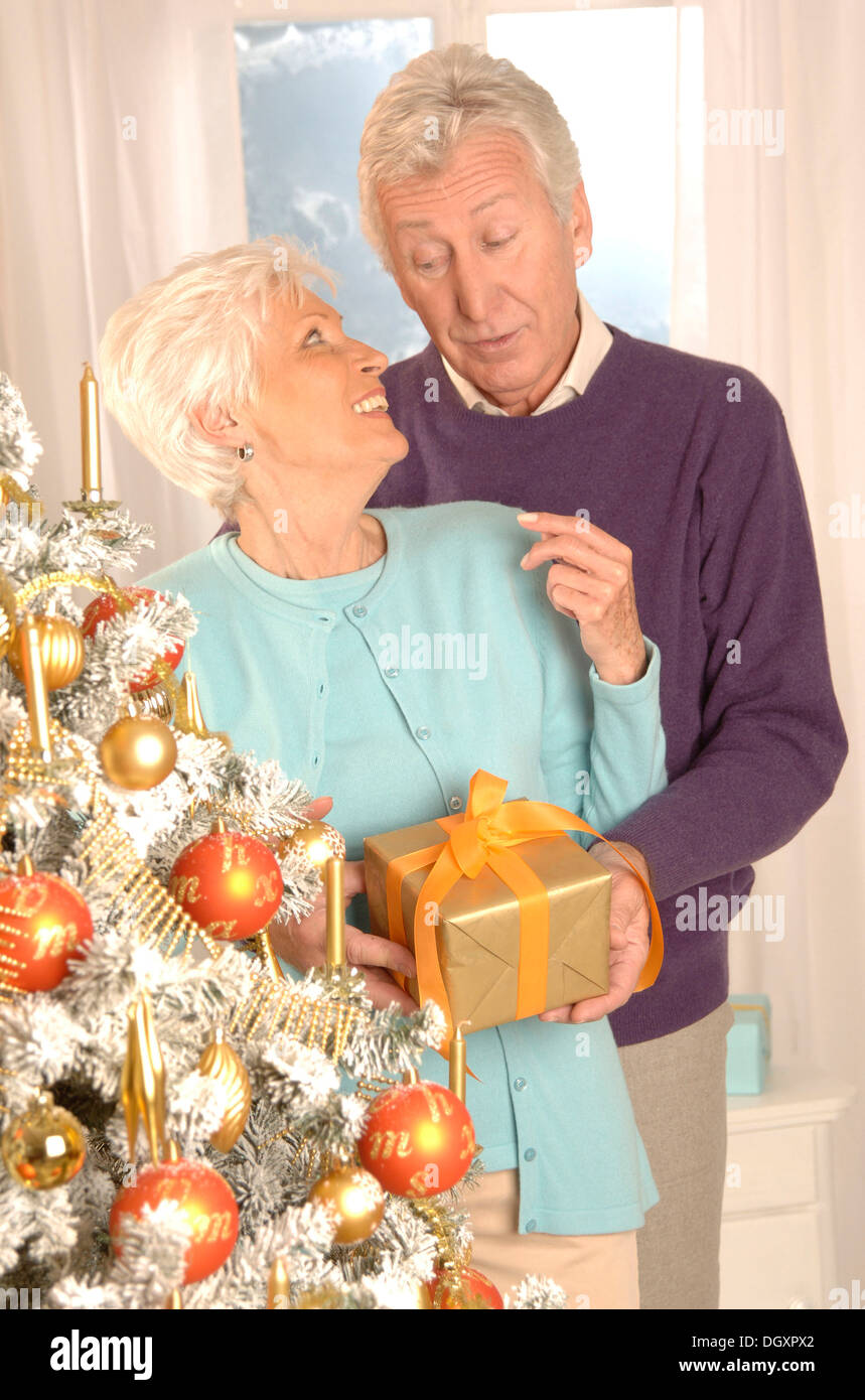 Mature couple with a present standing next to a Christmas tree Stock Photo