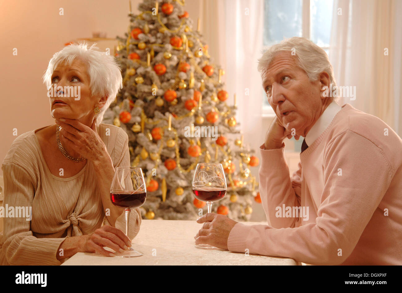 Mature couple sitting at a table with glasses of red wine, looking annoyed, in front of a Christmas tree Stock Photo