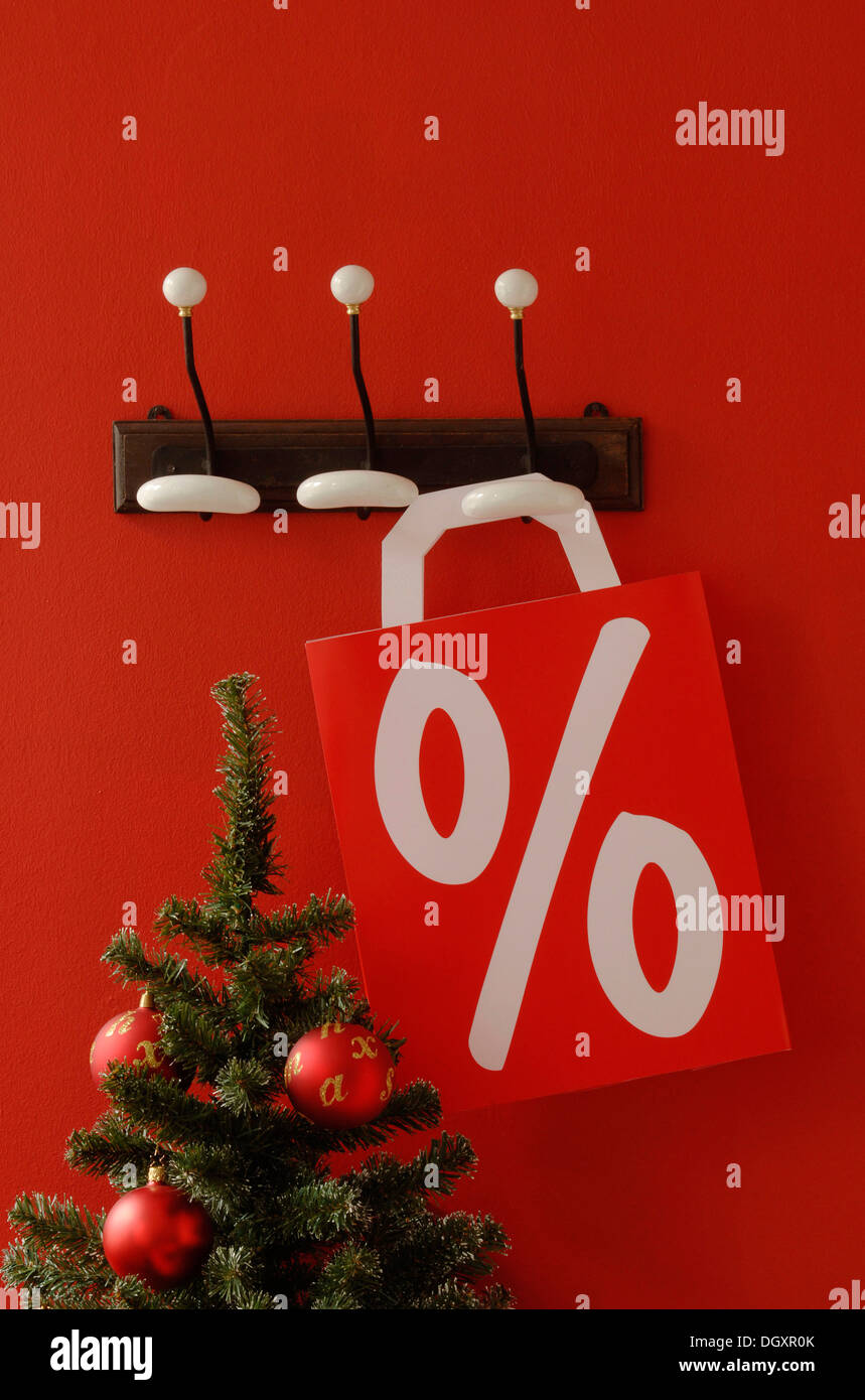 Shopping bag with per cent sign hanging on nostalgic coat hooks, Christmas tree at front Stock Photo