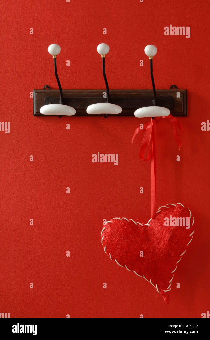 Red fabric heart hanging from nostalgic clothes hooks on a red wall Stock Photo