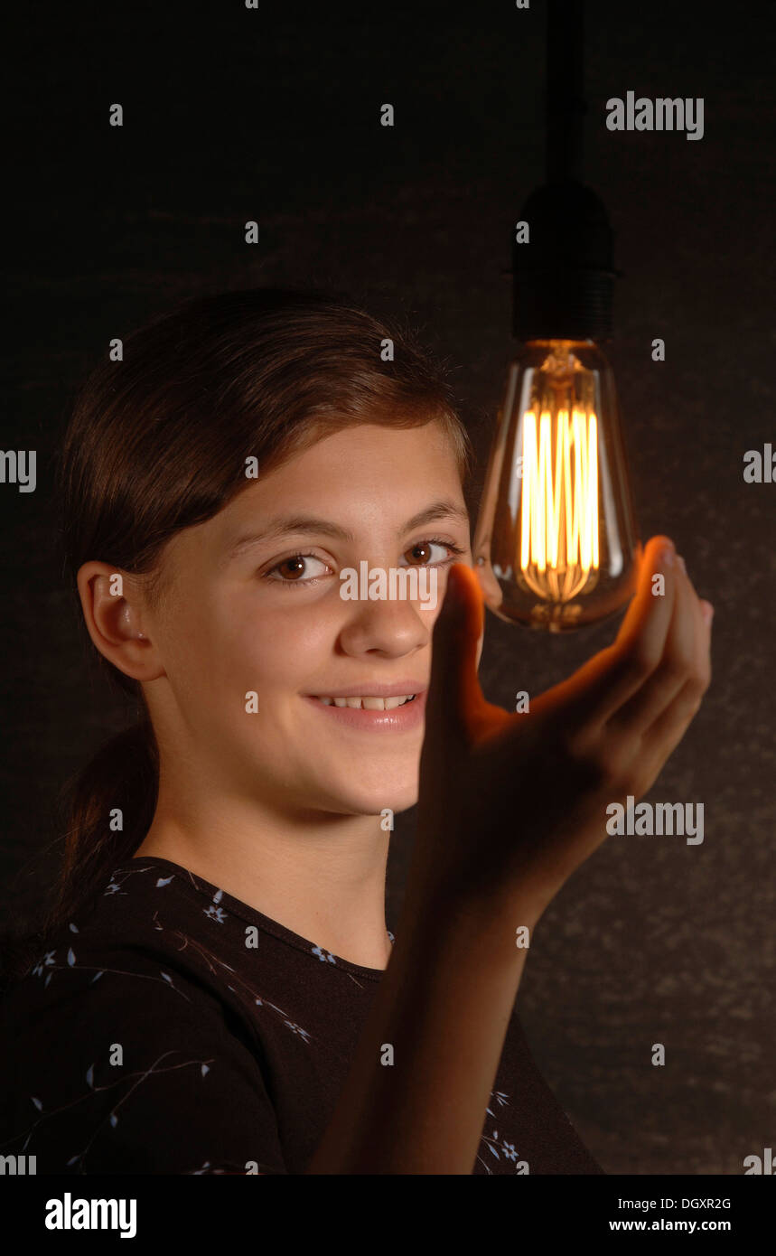 Smiling teenage girl holding a glowing light bulb in her hand Stock Photo
