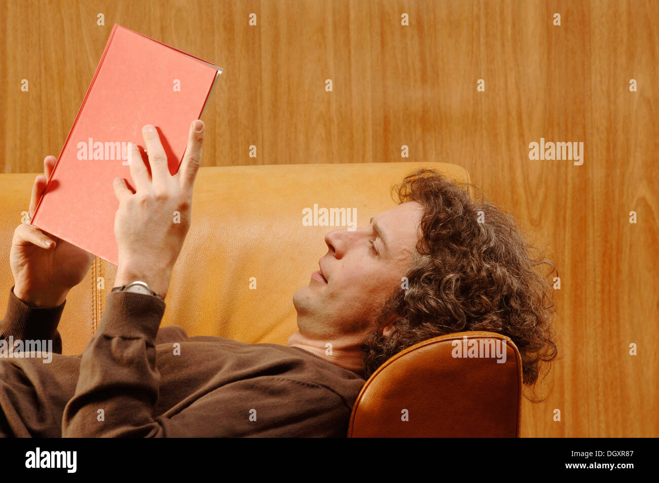 Man, 30-40, lying on a sofa, reading a red book Stock Photo