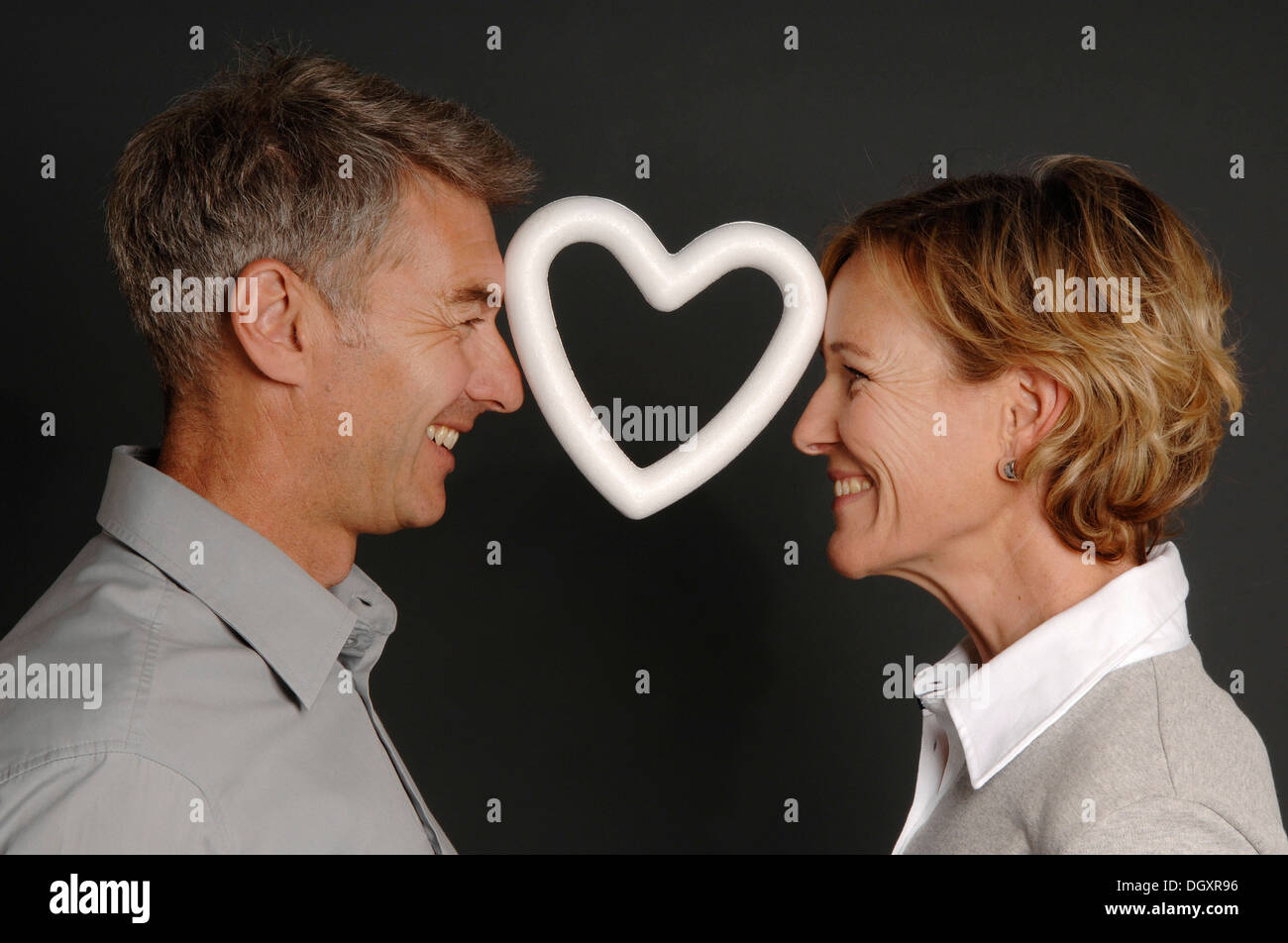 Couple, 35-45, standing face to face and holding a styrofoam heart between their foreheads Stock Photo