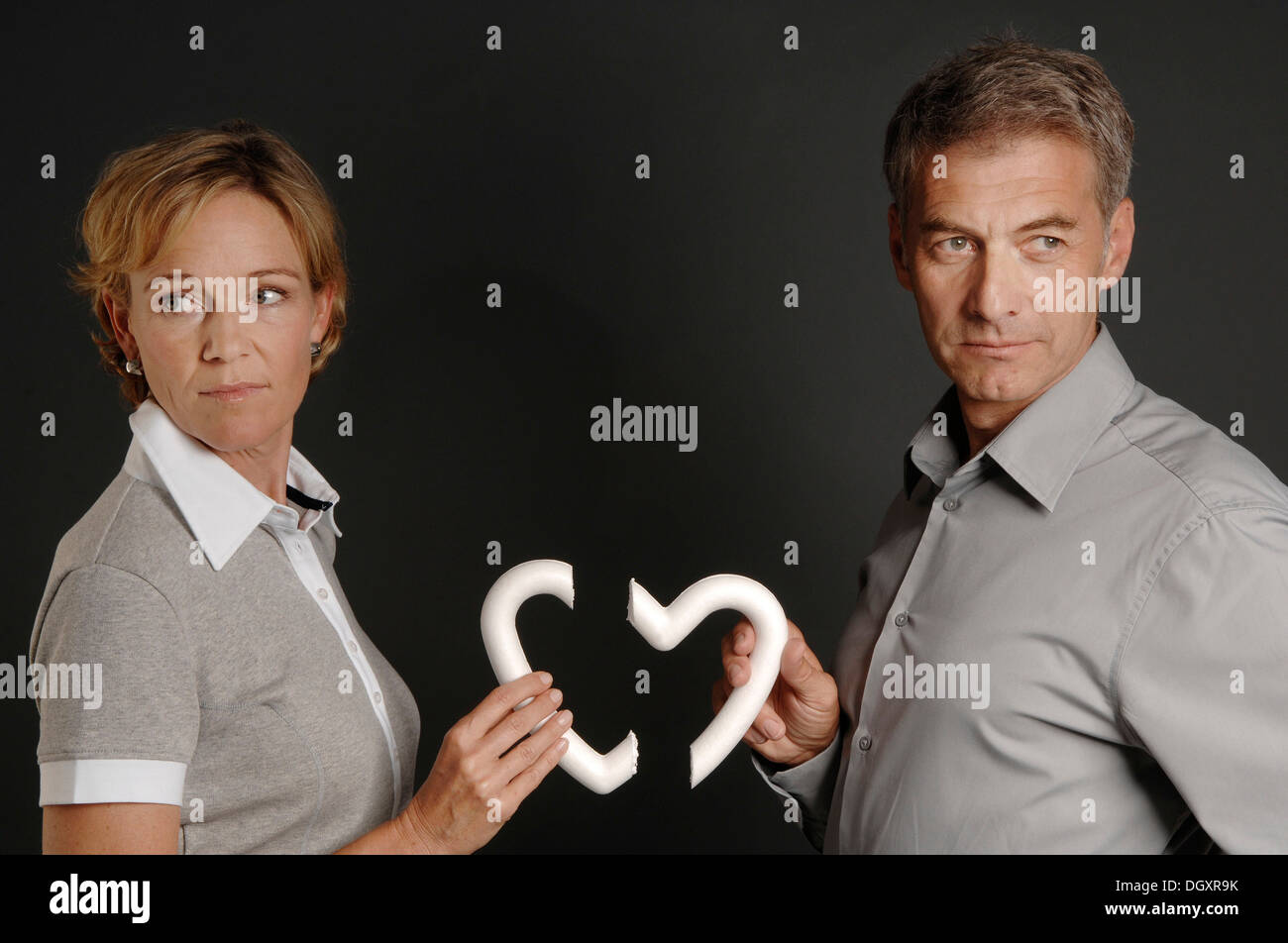 Men and women, 35-45, standing next to each other and holding a broken styrofoam heart in their hands Stock Photo