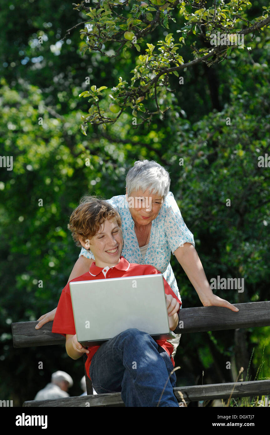 Grandson and grandmother looking together at a laptop computer on a park bench Stock Photo