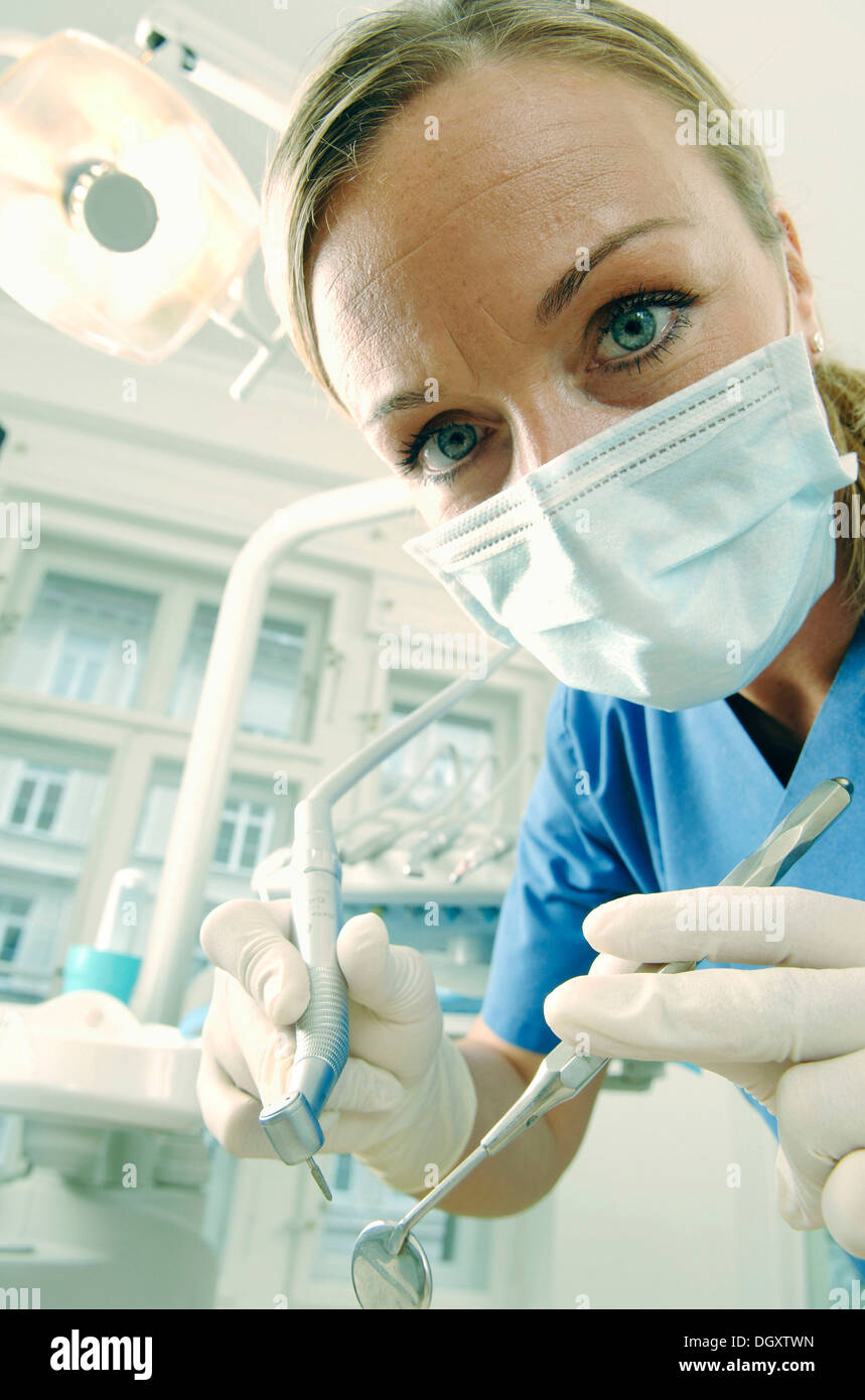 Dentist, dental hygienist, wearing a face mask in a treatment centre while holding a mirror and a drill Stock Photo