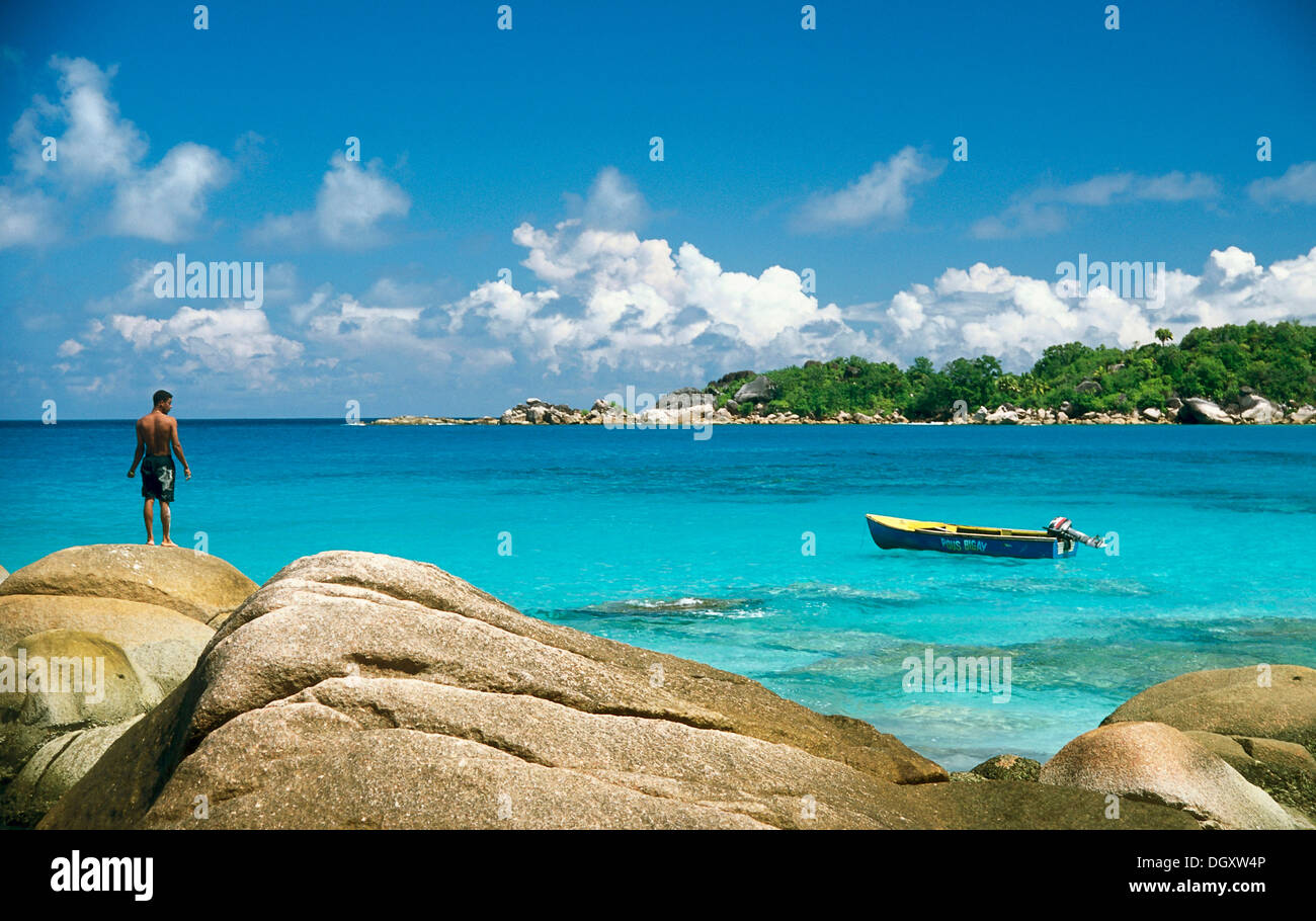 Rocky beach with a local fisherman and a fishing boat, Anse Lazio, Praslin, Seychelles Stock Photo