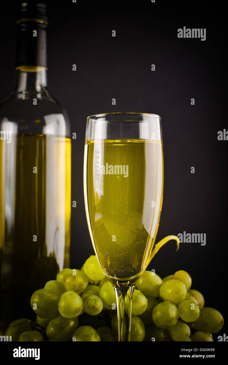 White wine in bottle and glass and white grapes on dark background