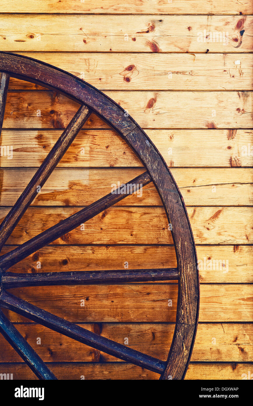 Old horse carriage wooden wheel leaning on the wooden wall Stock Photo