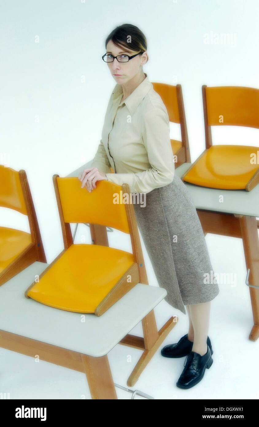Strict female teacher standing at old school desks with orange chairs Stock Photo