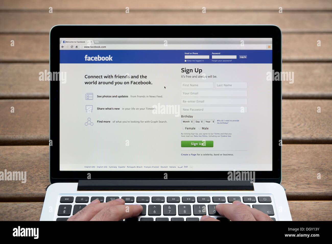 The Facebook website on a MacBook against a wooden bench outdoor background including a man's fingers (Editorial use only). Stock Photo