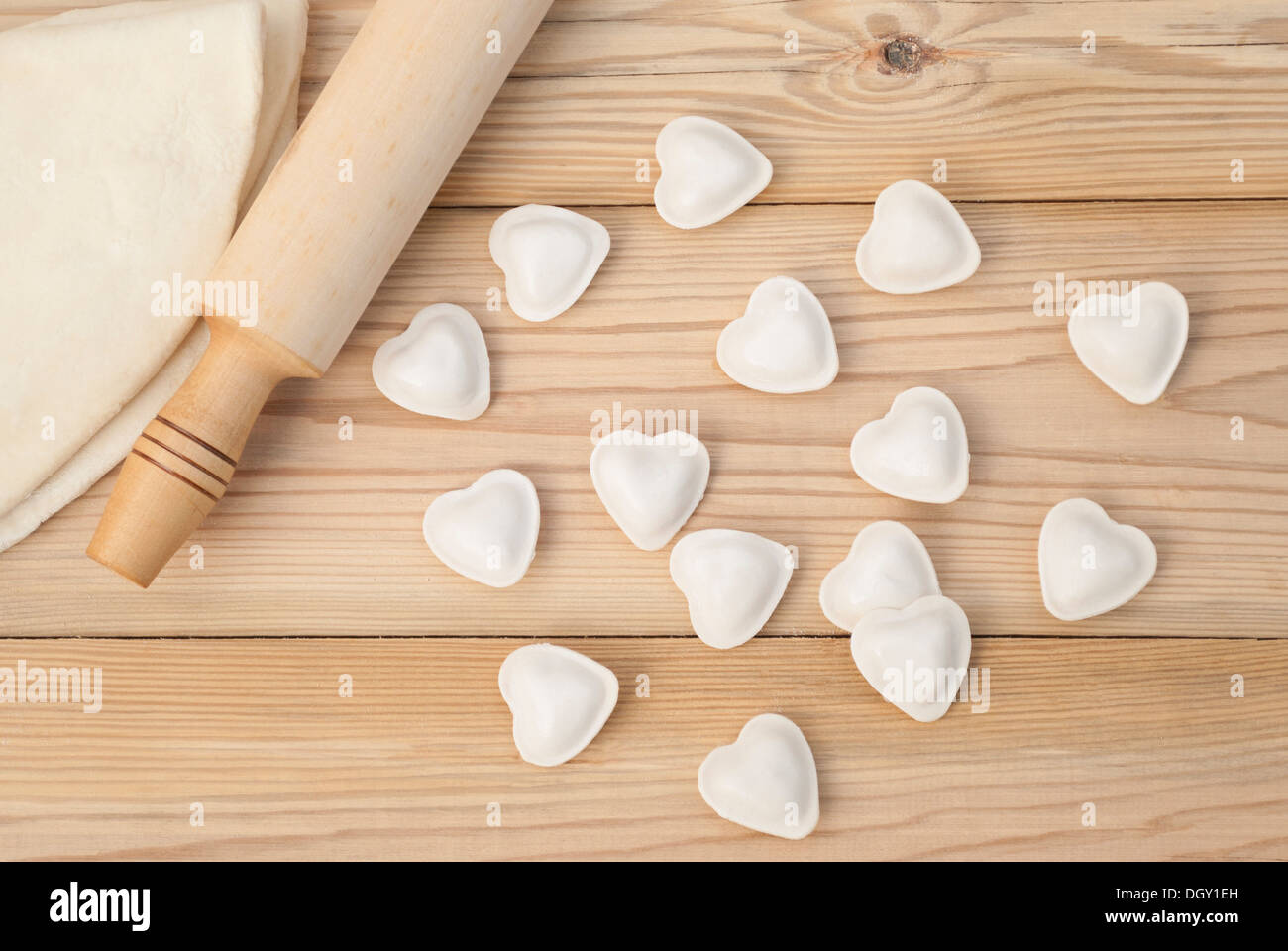 Dumplings in a heart shape dough and rolling pin on the wooden table. Stock Photo
