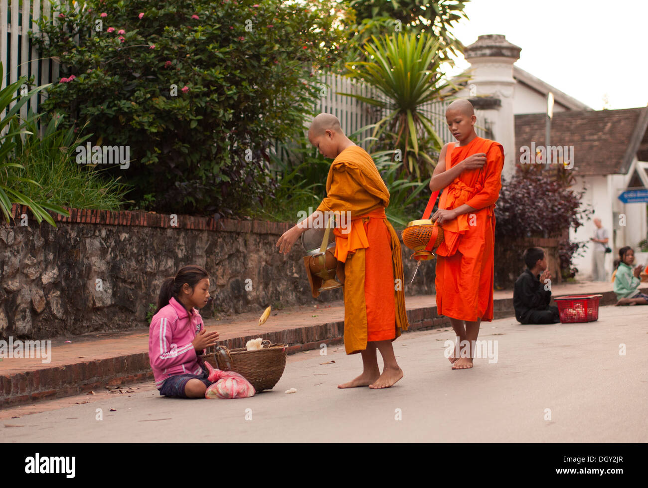 A Buddhist monk gives a poor girl food during the daily morning ceremony of giving alms to monks in Luang Prabang, Laos. Stock Photo