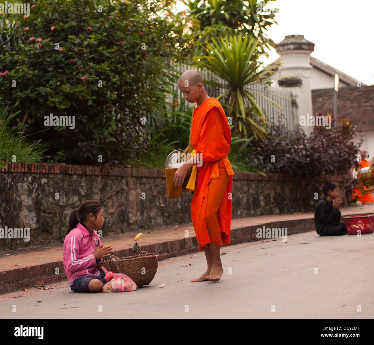 A Buddhist monk gives a poor girl food during the daily morning ceremony of giving alms to monks in Luang Prabang, Laos. Stock Photo