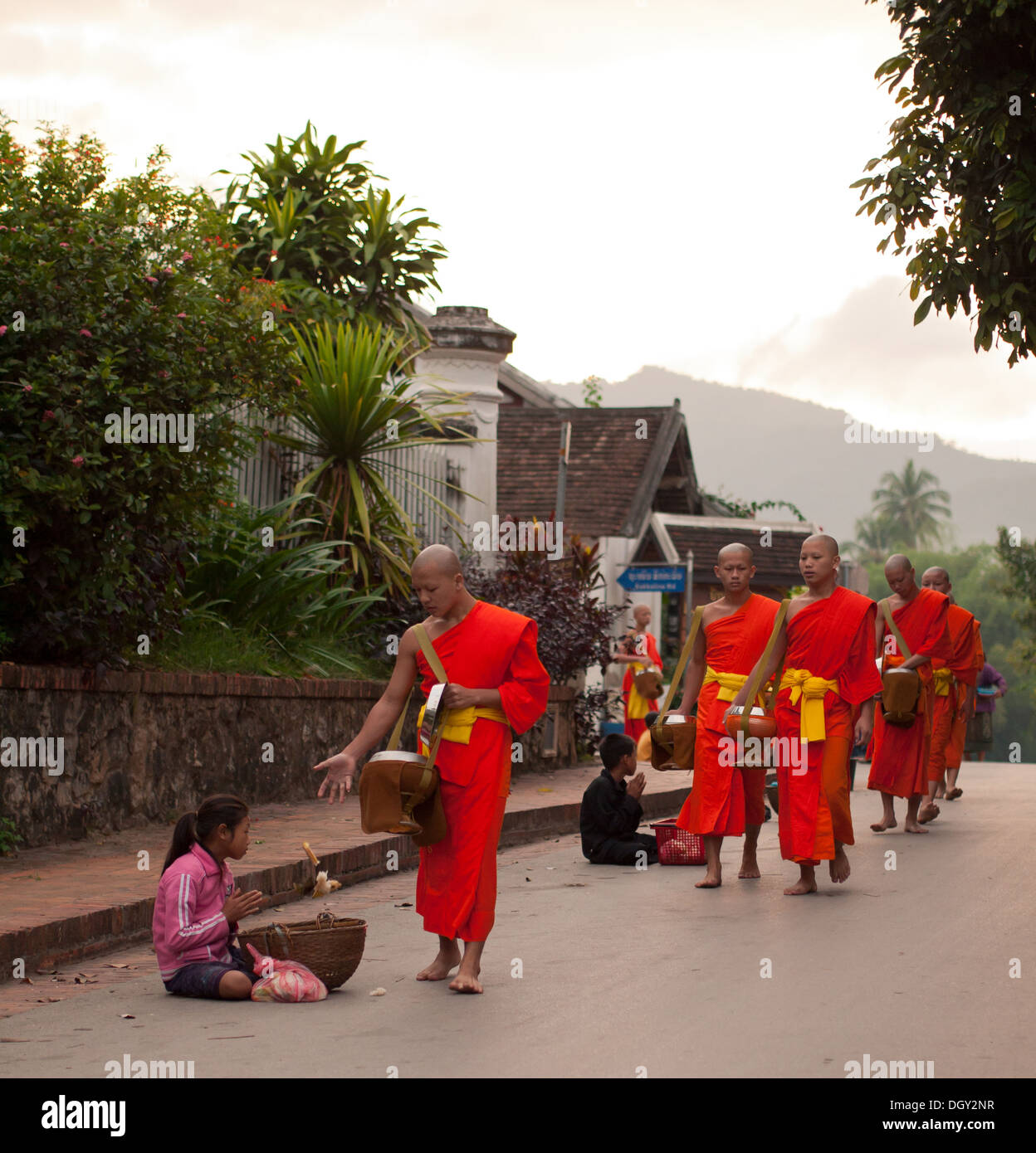 A Buddhist monk gives a poor girl food during the daily morning ceremony of giving alms to monks in Luang Prabang, Laos. Stock Photo