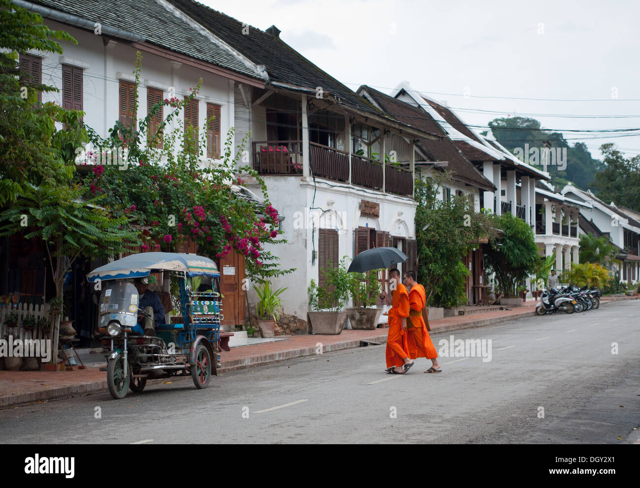 A view of a parked Laotian tuk-tuk and two Buddhist monks crossing Sakkaline Road in Luang Prabang, Laos. Stock Photo
