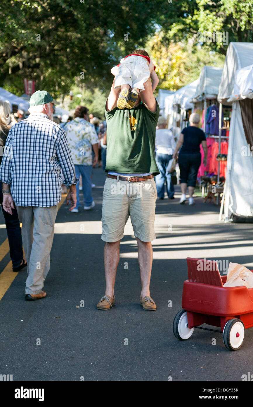 Father man holds or tosses young son boy child into air at the Mount Dora Crafts Fair Festival in Florida. Stock Photo