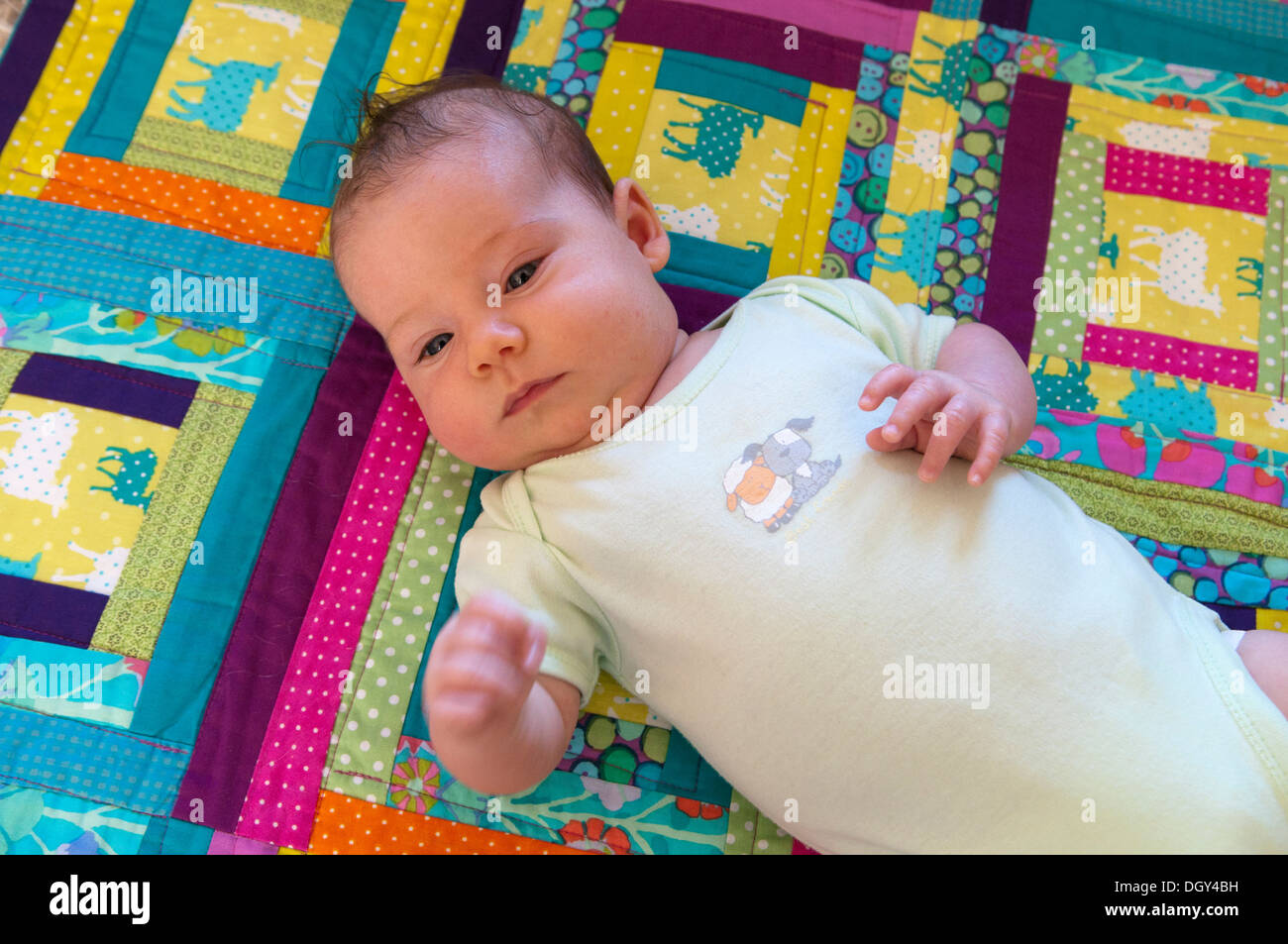 Little baby girl lying down on a colourful patchwork quilt Stock Photo