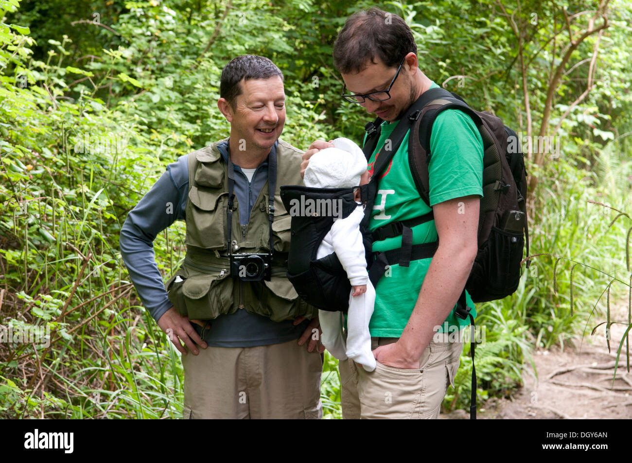 Father and son carrying his little baby in a sling enjoying a walk in the countryside Stock Photo