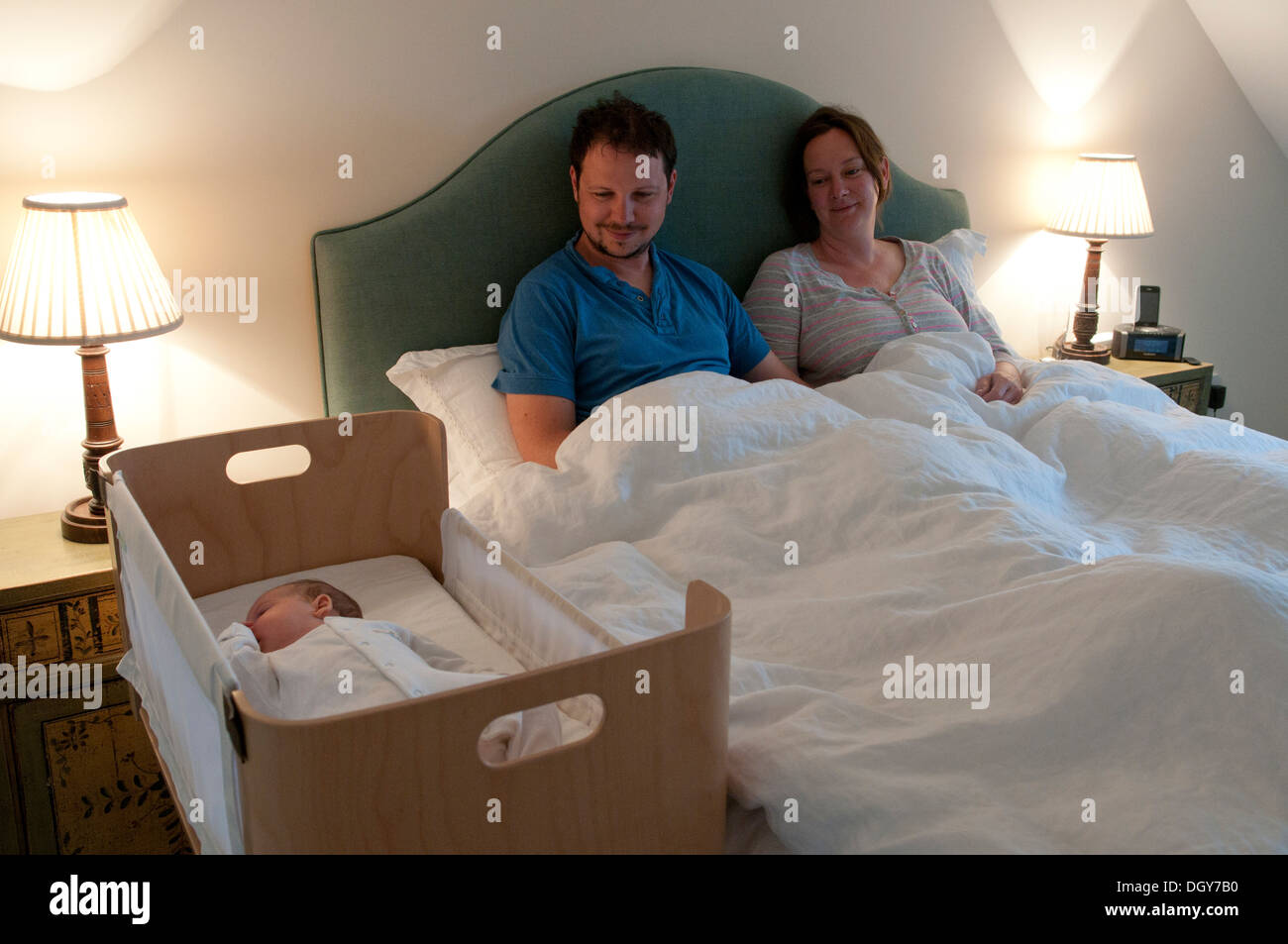 New parents in bed awake smiling and looking at their baby girl sleeping Stock Photo