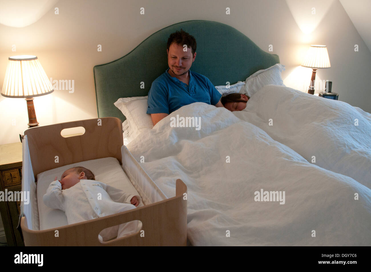 New parents in bed, mum asleep, dad awake watching their baby girl Stock Photo