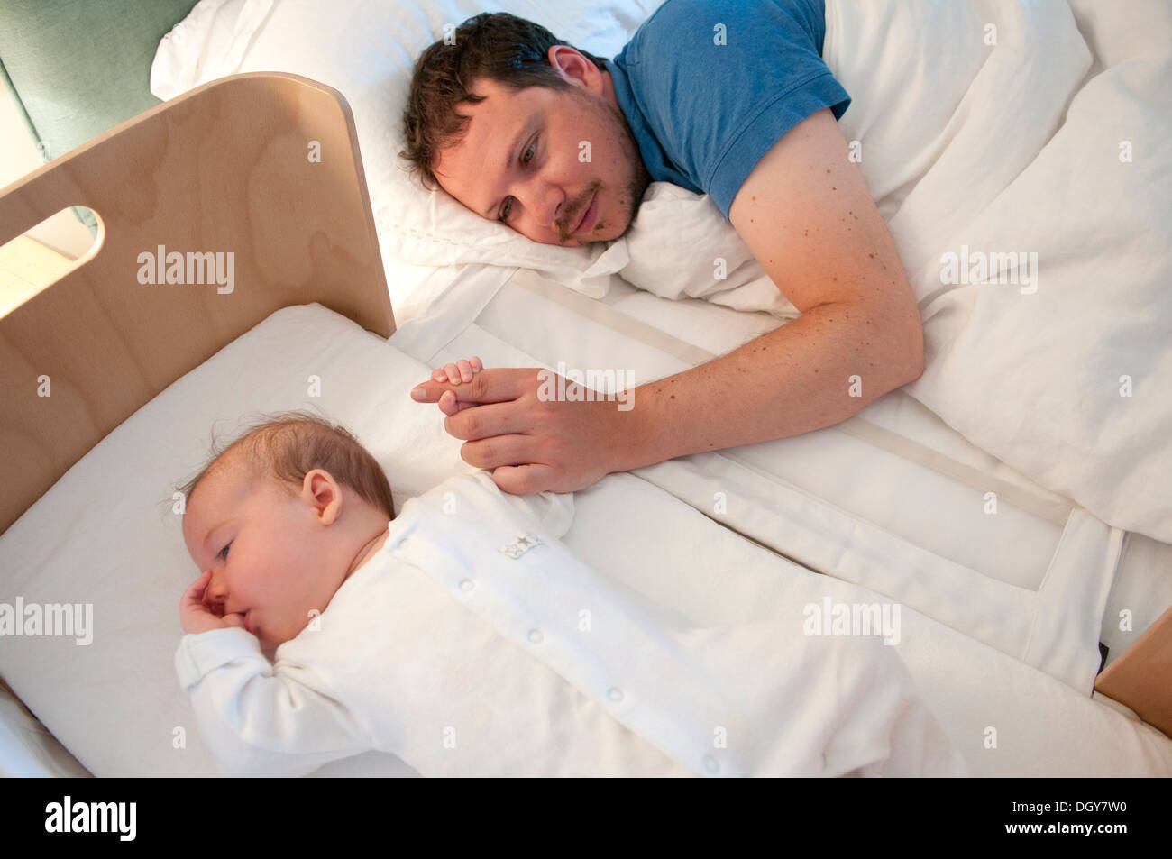 New father in bed comforting his little baby girl and holding her hand Stock Photo