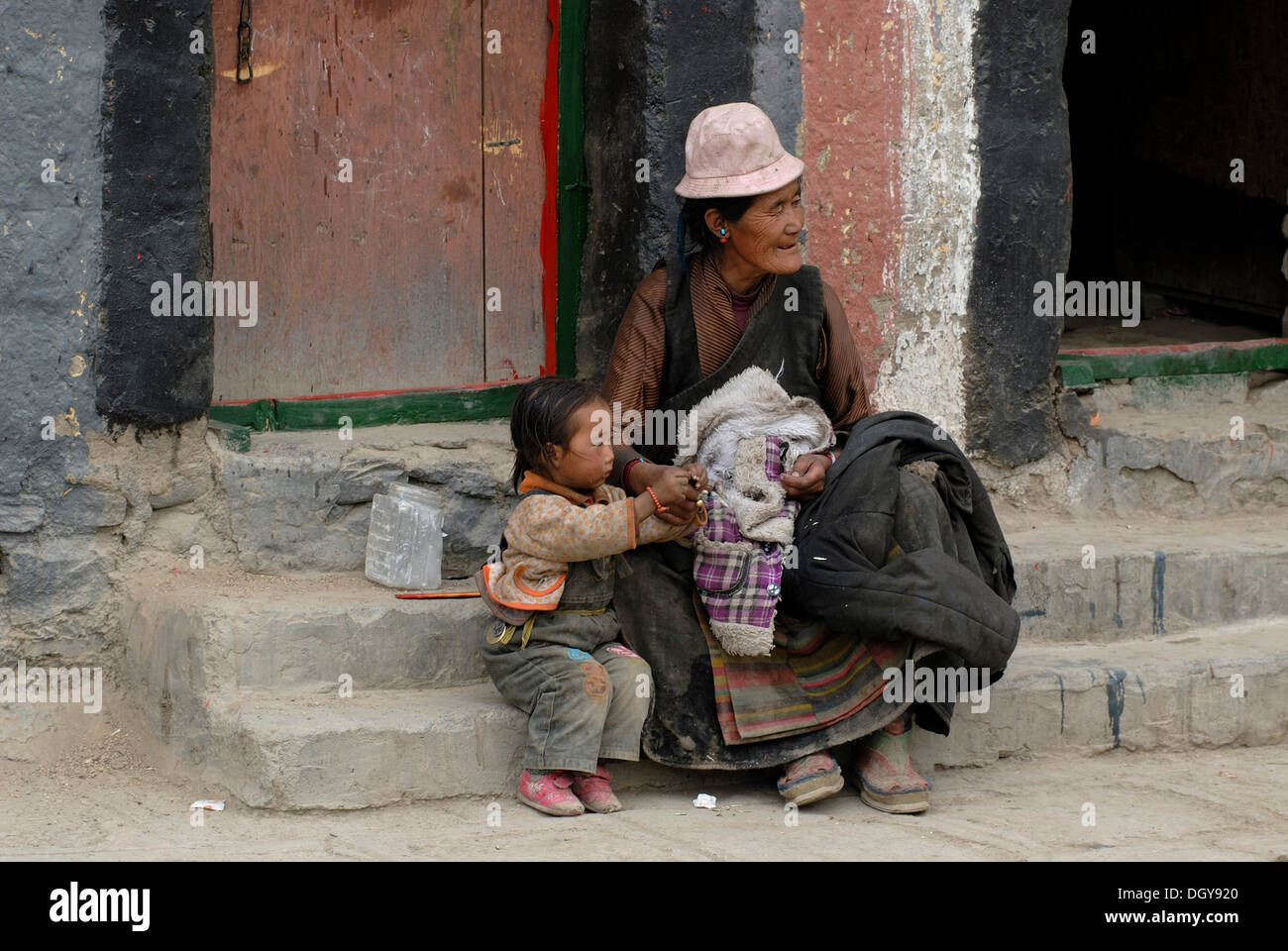 Tibetan grandmother with grandchildren in the monastery-town of Sakya in front of a typical Sakya building construction and Stock Photo