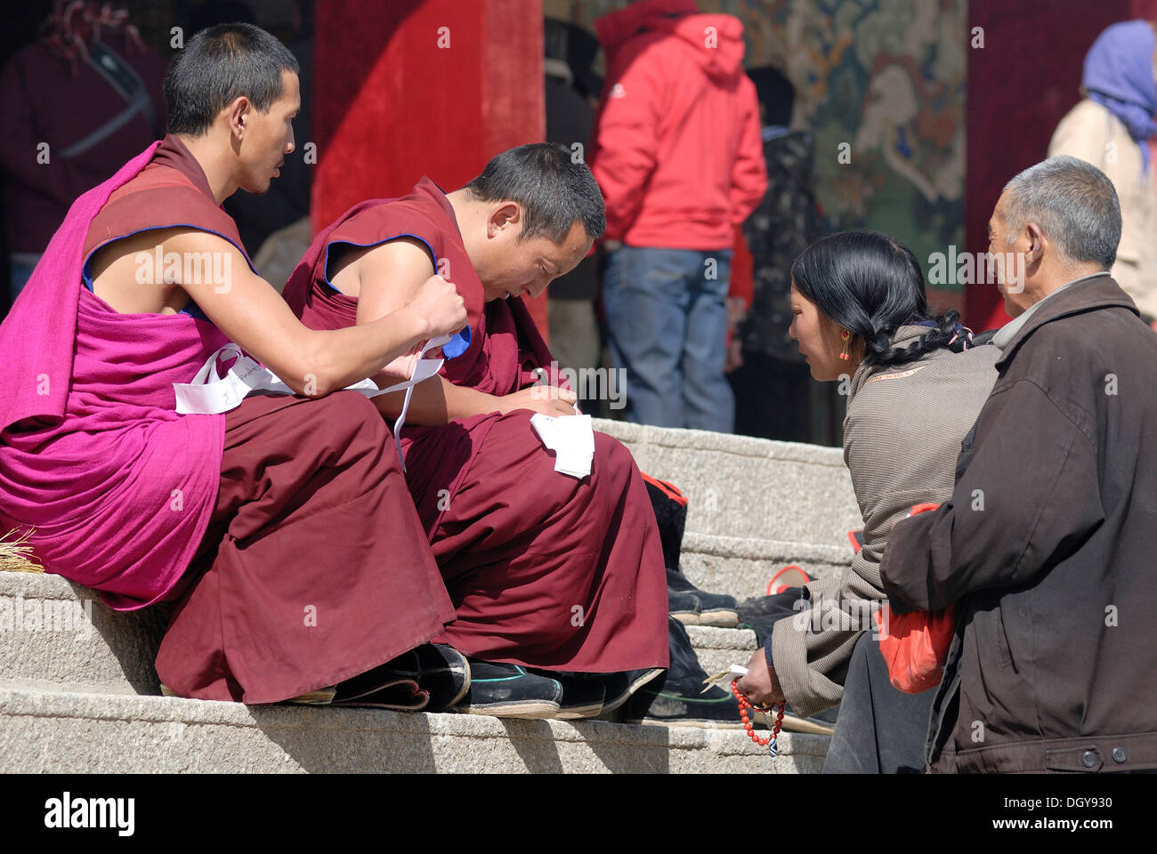 Tibetan monks in monk's robes of the Gelukpa order talking with Tibetan pilgrims, on the stairs in front of the meeting hall or Stock Photo