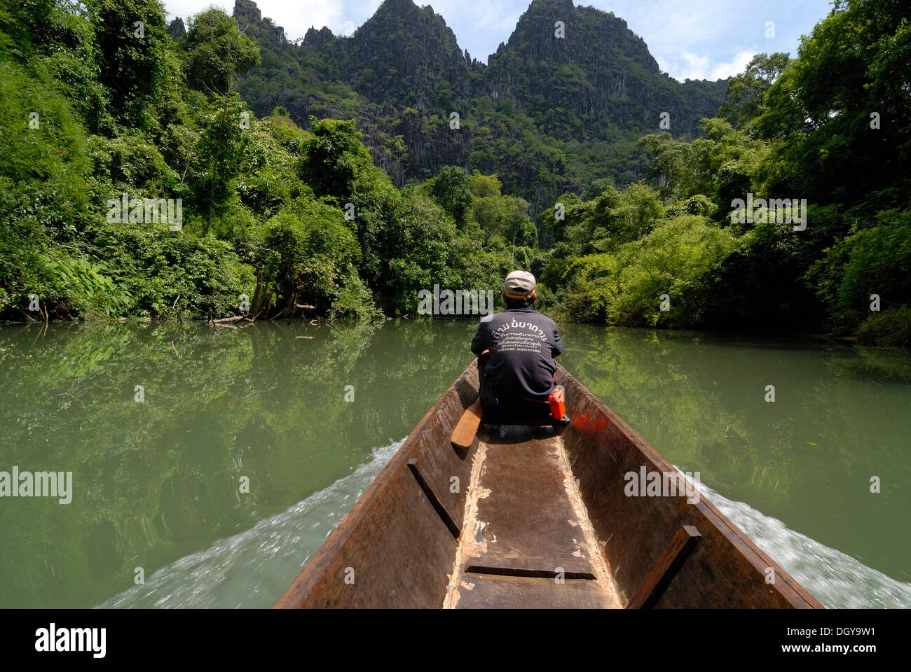 Laotian man with a simple long boat at the entrance of the 7.5 km long cave of Tham Kong Lor, amidst the dense subtropical Stock Photo