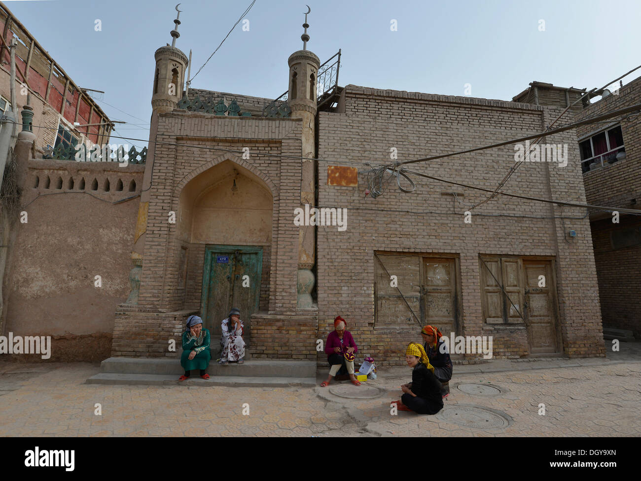 Muslim women, Uighurs with colourful headscarves sitting in front of a mosque, mud-brick houses, Uighur historic centre of Stock Photo