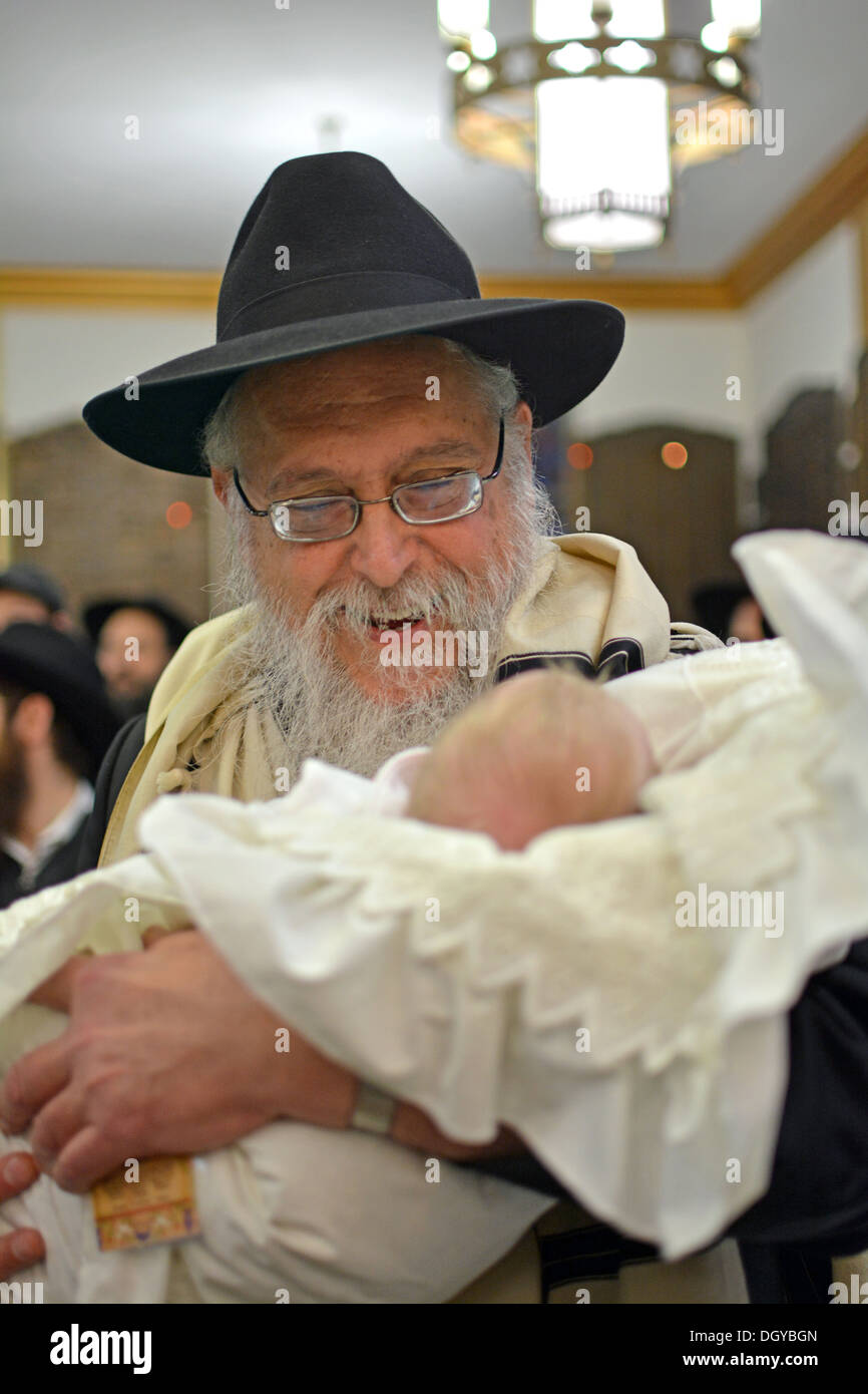 Religious Jewish grandfather holding his grandson at a bris 