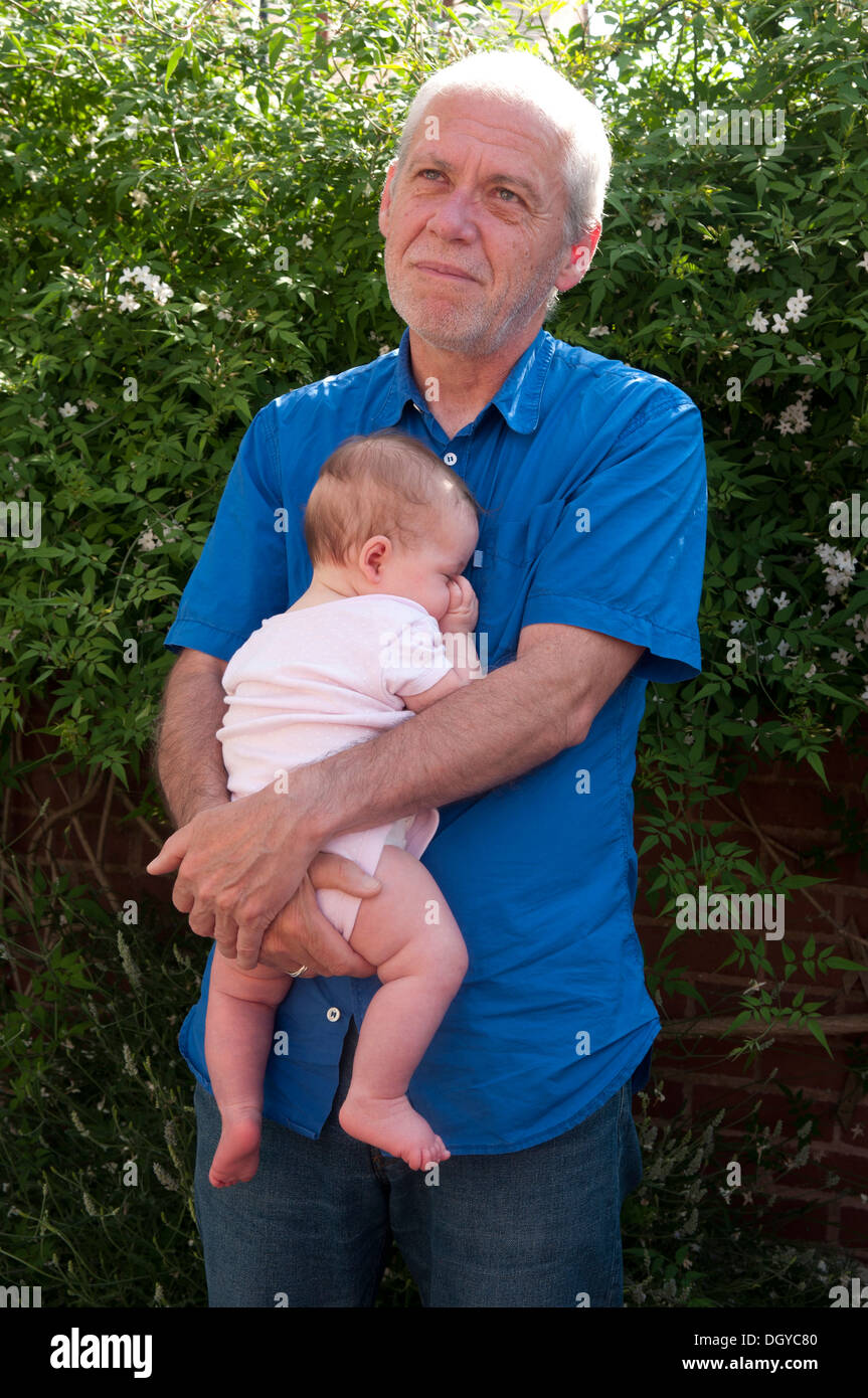Little baby girl being held by her grandfather sleeping and sucking her thumb Stock Photo