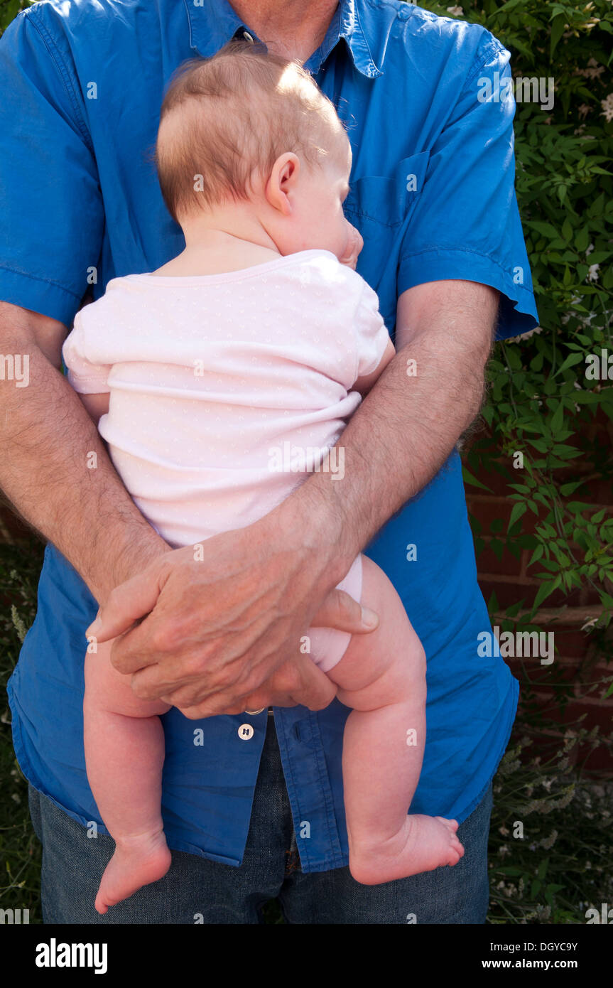 Back view of a little baby girl being held sleeping and sucking her thumb Stock Photo
