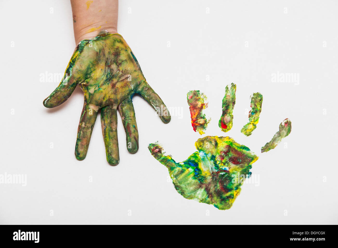 Child with colorful painted hand beside her hand print on paper Stock Photo