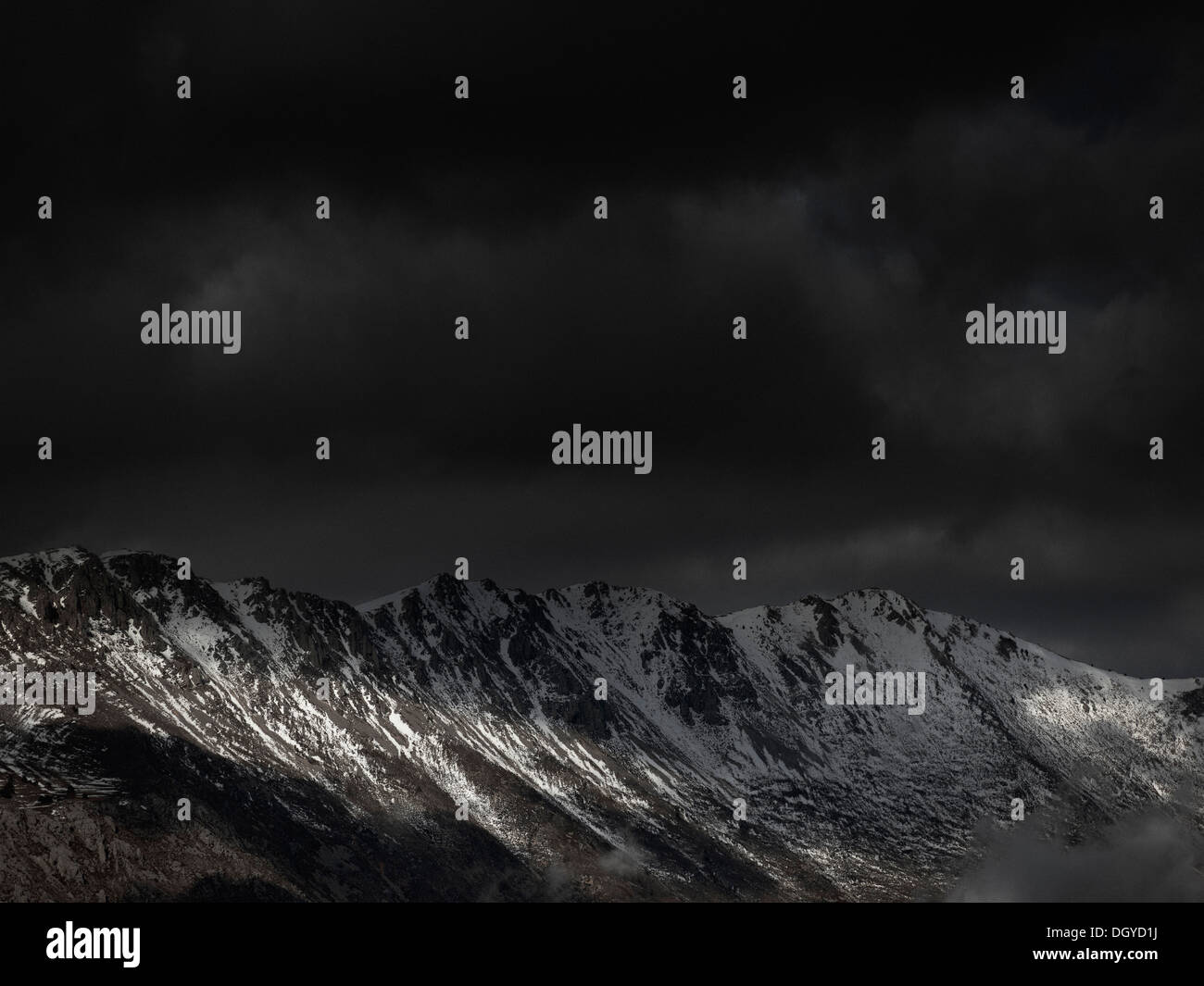 An ominous sky with some sunlight breaking through over a mountain range Stock Photo