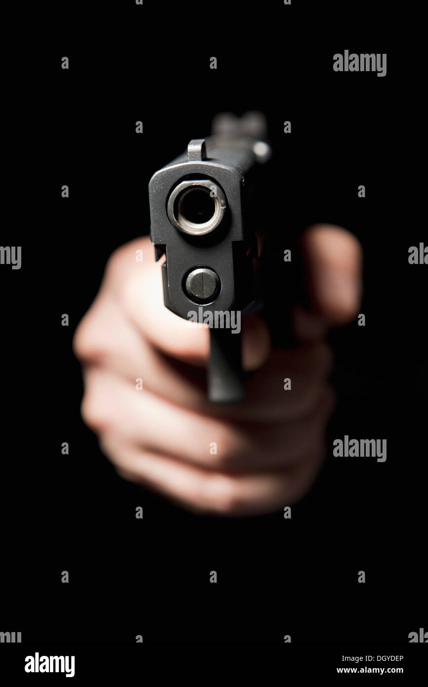 A hand holding a gun and pointing it at the camera, black background Stock Photo