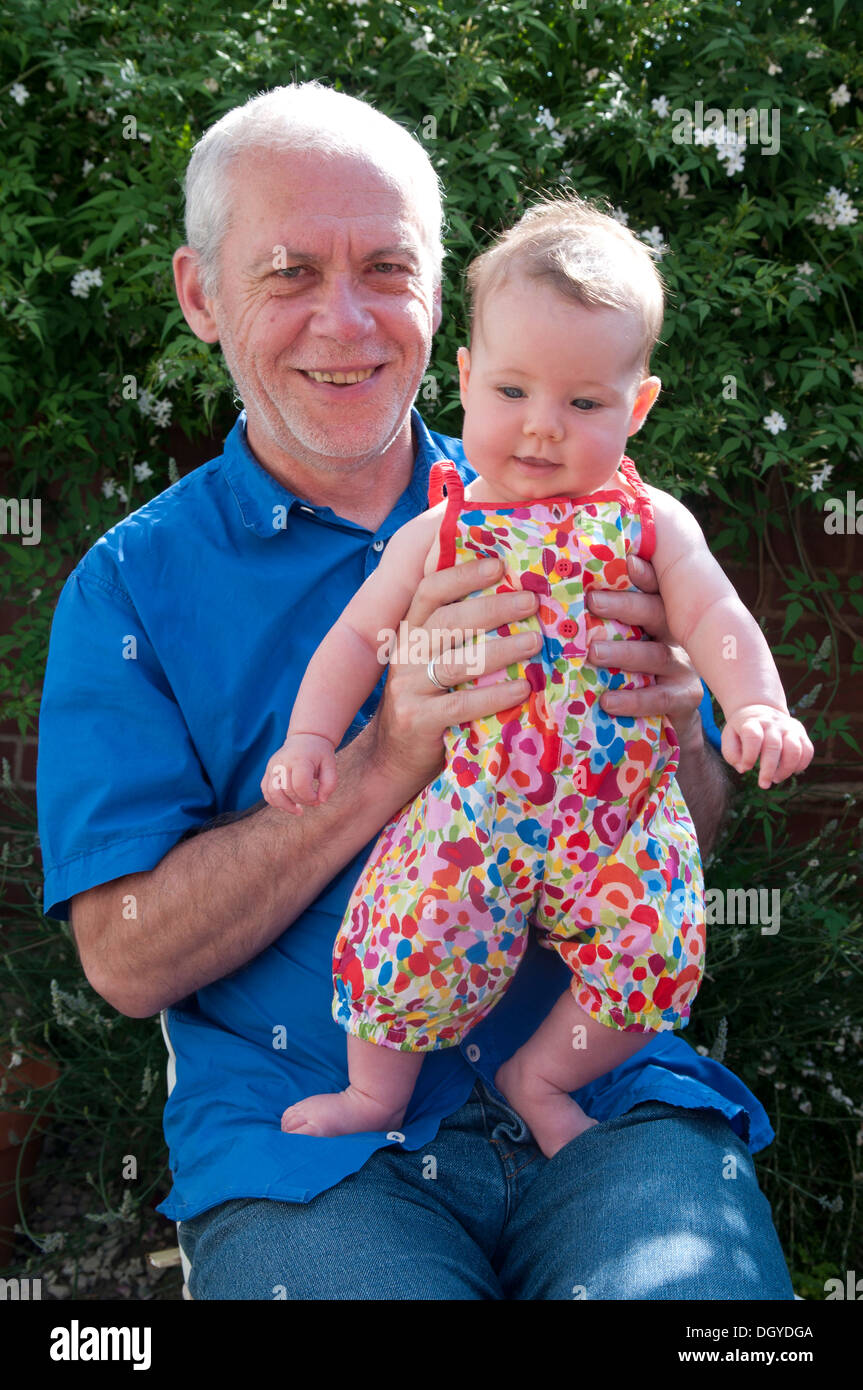 Little baby girl being held by her grandfather smiling, sitting outside in the garden Stock Photo
