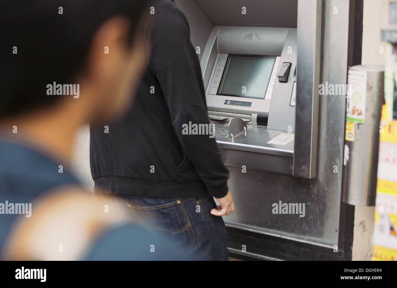 Man using a bank atm machine on the street with a thief watching him from behind Stock Photo